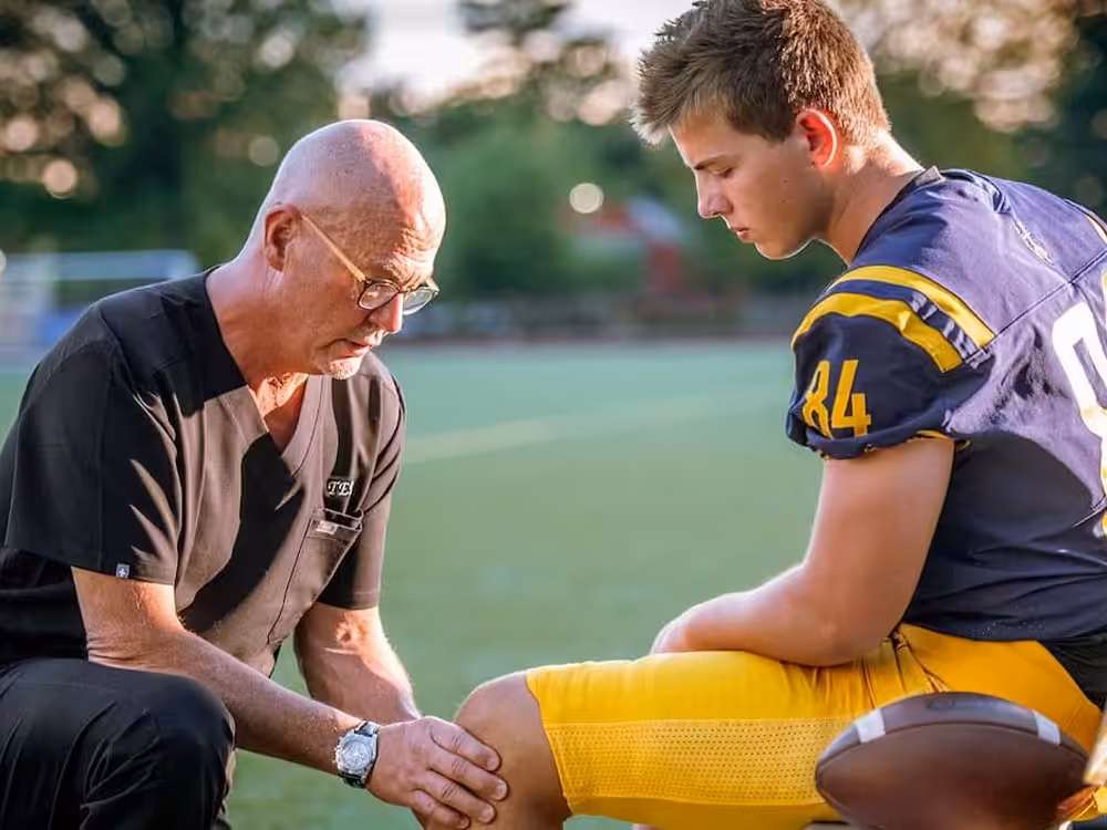 Sports Beacon Orthopedics doctor seen with football player, analyzes athletes knee on the football