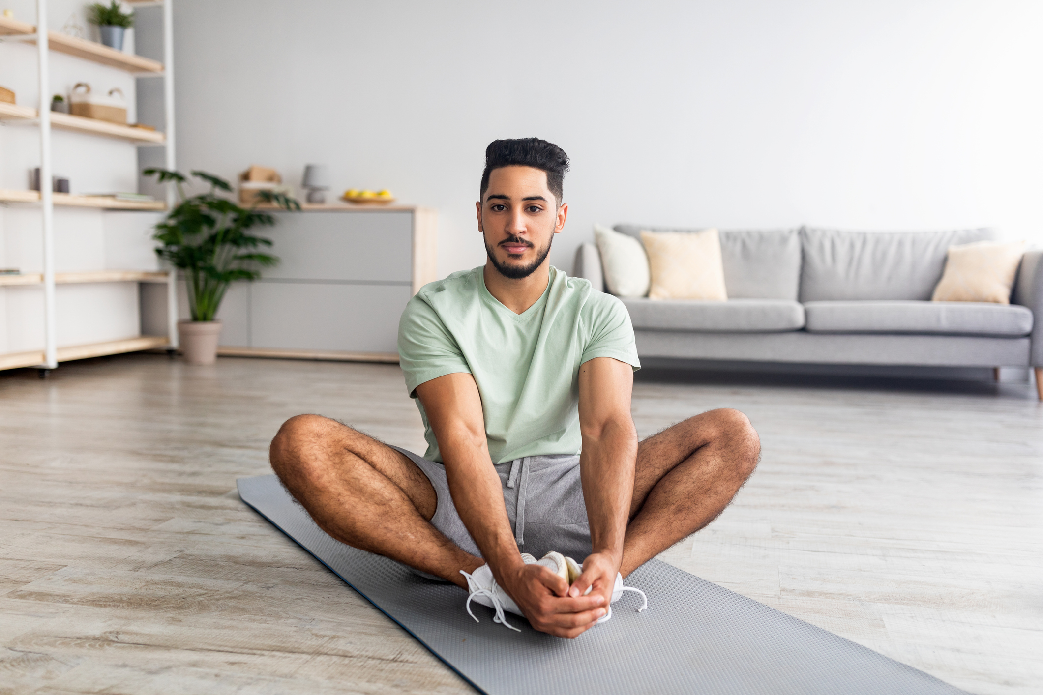 Home workout. Sporty young guy butterfly stretching on mat in living room, practicing yoga, full length. 